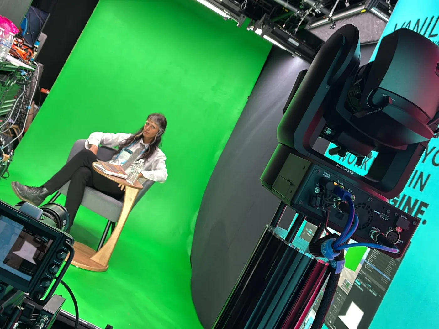 A green-screen studio: a presenter seated on set, the Lift and its PTZ camera framing them.